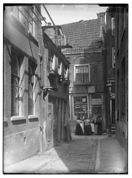 Voorbeeld van een Water- en Vuurhuisje.  <p>Water-en-vuur winkeltje in de Blindemansteeg (1907-1917) gezien vanaf de Reguliersdwarsstraat naar winkel De Morgenstond, Blindemansteeg 19, met een groepje vrouwen. Een bord boven de ingang maakt reclame voor poppenspeler A.A. van Hemert. Op de voorgrond links de zijgevel van Reguliersdwarsstraat 107.<br />Bron: Beeldbank Stadsarchief Amsterdam.</p>