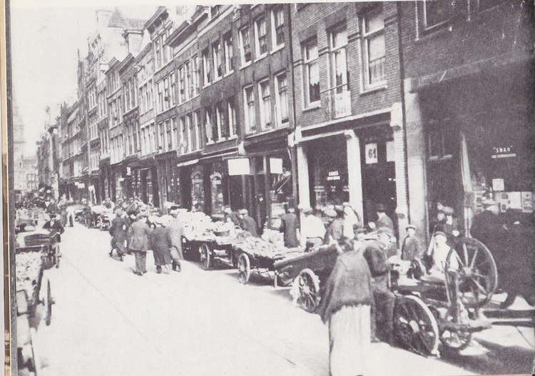 Jodenbreestraat nummer 63 en lager.  <p>Deze foto is uit het jaar 1909. Volgens M.H.Gans is er hier sprake van de markt voor Pesach. Duidelijk is dat de Jodenbreestraat meer is dan een winkelstraat. De markt was tegenover de Mozes en Aäronkerk, er werd vooral serviesgoed verkocht. Bron: De Amsterdamse Jodenhoek in foto's. M.H.Gans, uitg. Ten Have BV, Baarn 1974. De herkomst van de foto is onbekend.</p>