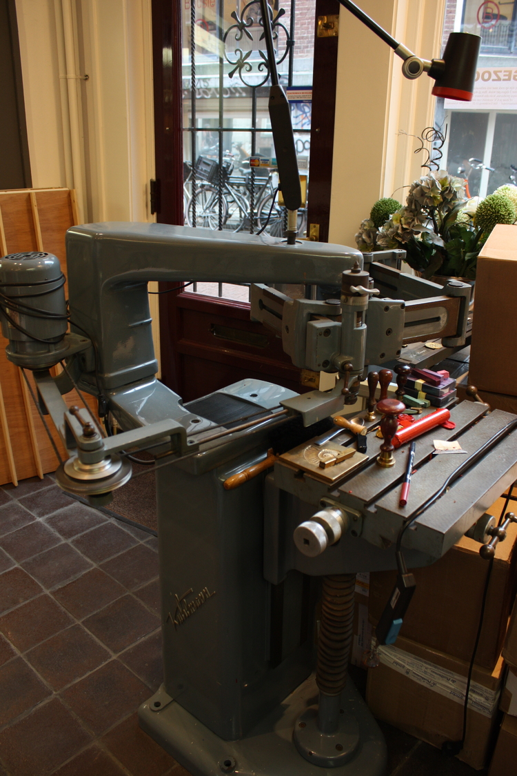Posthumuswinkel: oude stempelmachine  <p>De oude machine waarmee vroeger de stempels werden gemaakt staat prominent in beeld.</p>