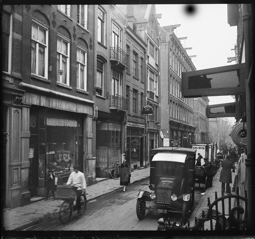 Rapenburg 86, 84, 82 enz. met links de zaak van A. van Gelder, 2 huizen verder het café van J.J. van der Veer. In de straat auto's en een bakfiets (1930), Bron: Beeldbank SAA.  